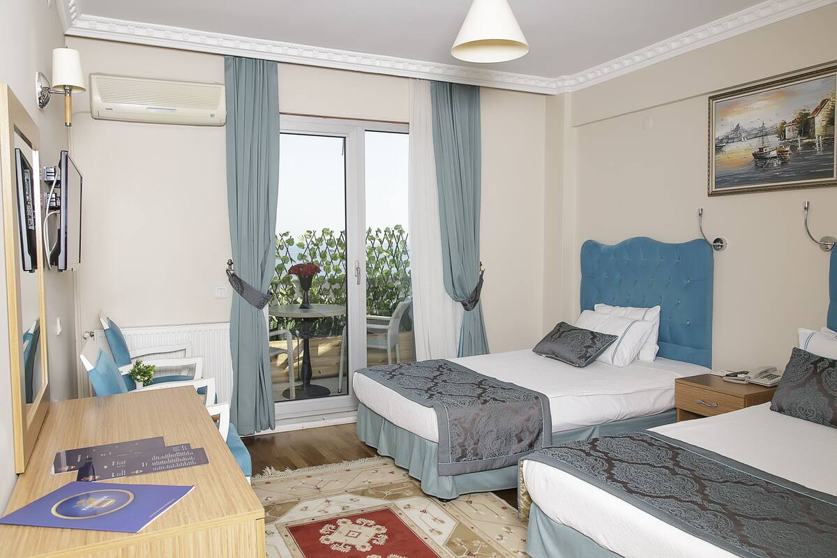 A hotel room with two beds, a desk, a chair, a table, and a balcony with a view.