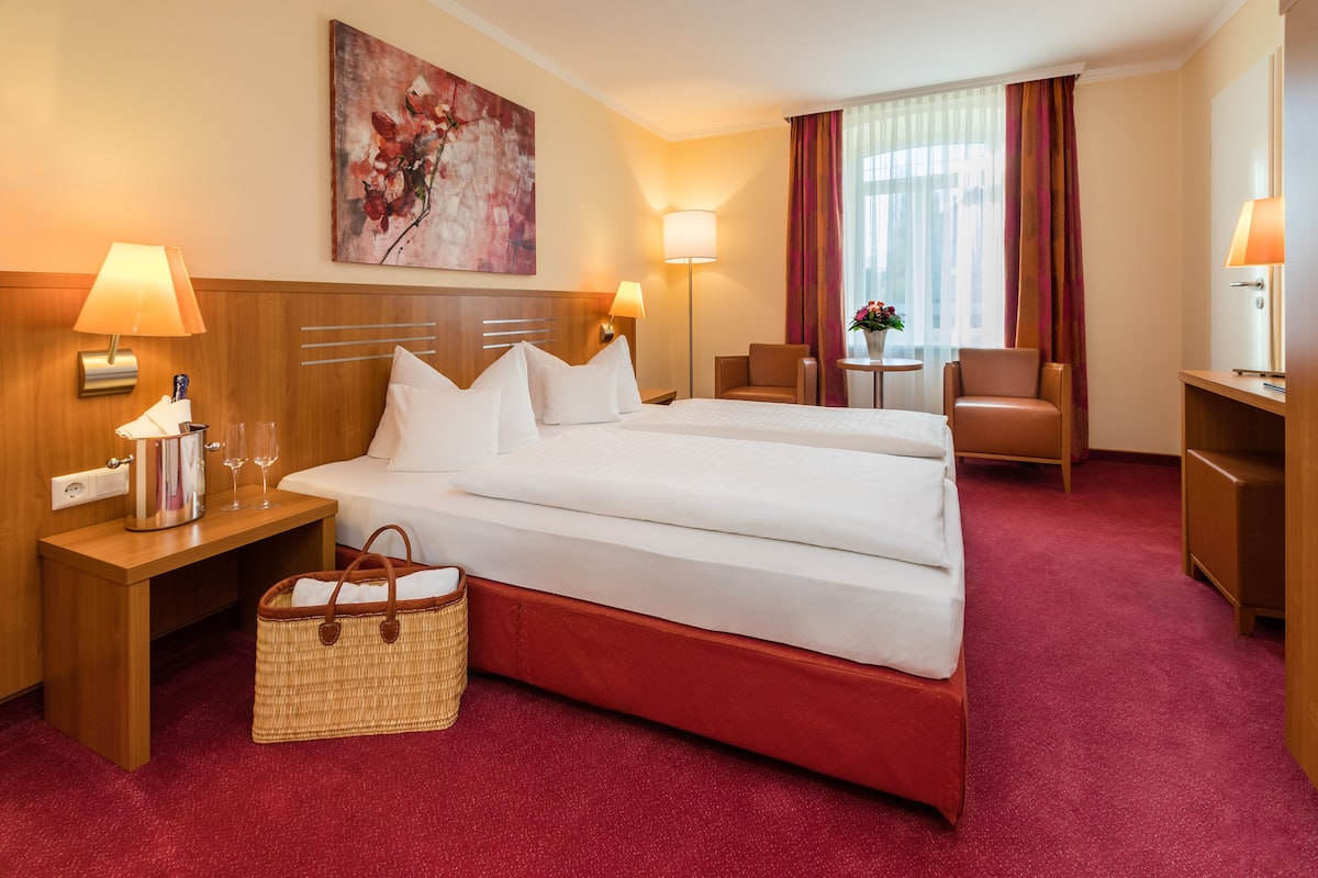 A hotel room with a large bed, bedside tables, a lamp, a small table with a vase, and a chair.