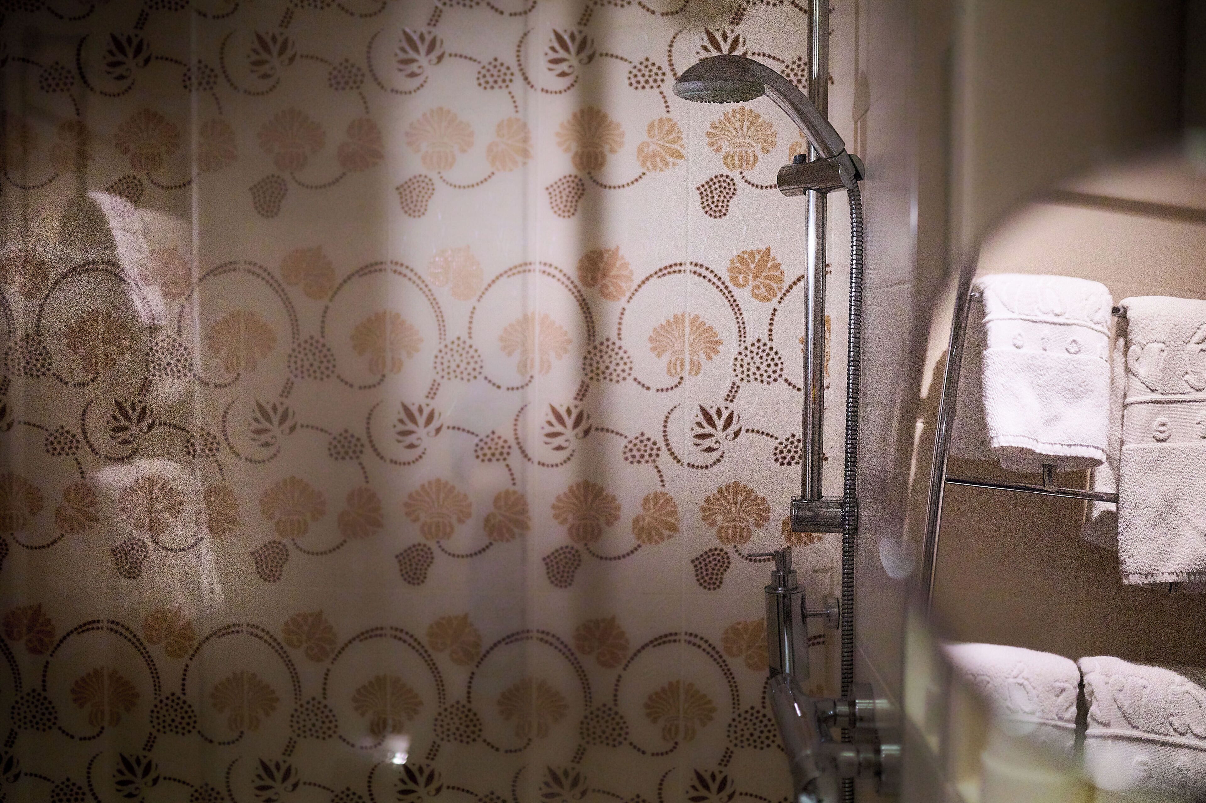 A shower with a floral pattern curtain, a handheld showerhead, and a towel rack with towels.