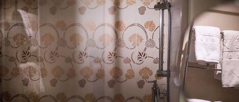 A shower with a floral pattern curtain, a handheld showerhead, and a towel rack with towels.
