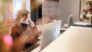 Una persona sentada en un escritorio con una computadora, un teléfono y una lámpara.