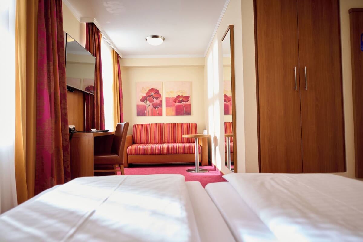 A hotel room with two beds, a desk, a chair, a sofa, and a wardrobe.