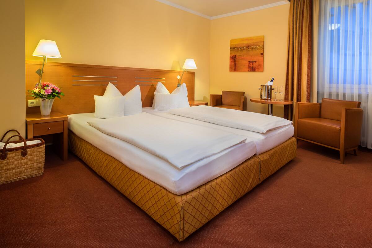 A hotel room with a large bed, two bedside tables, a chair, a desk, and a window with curtains.