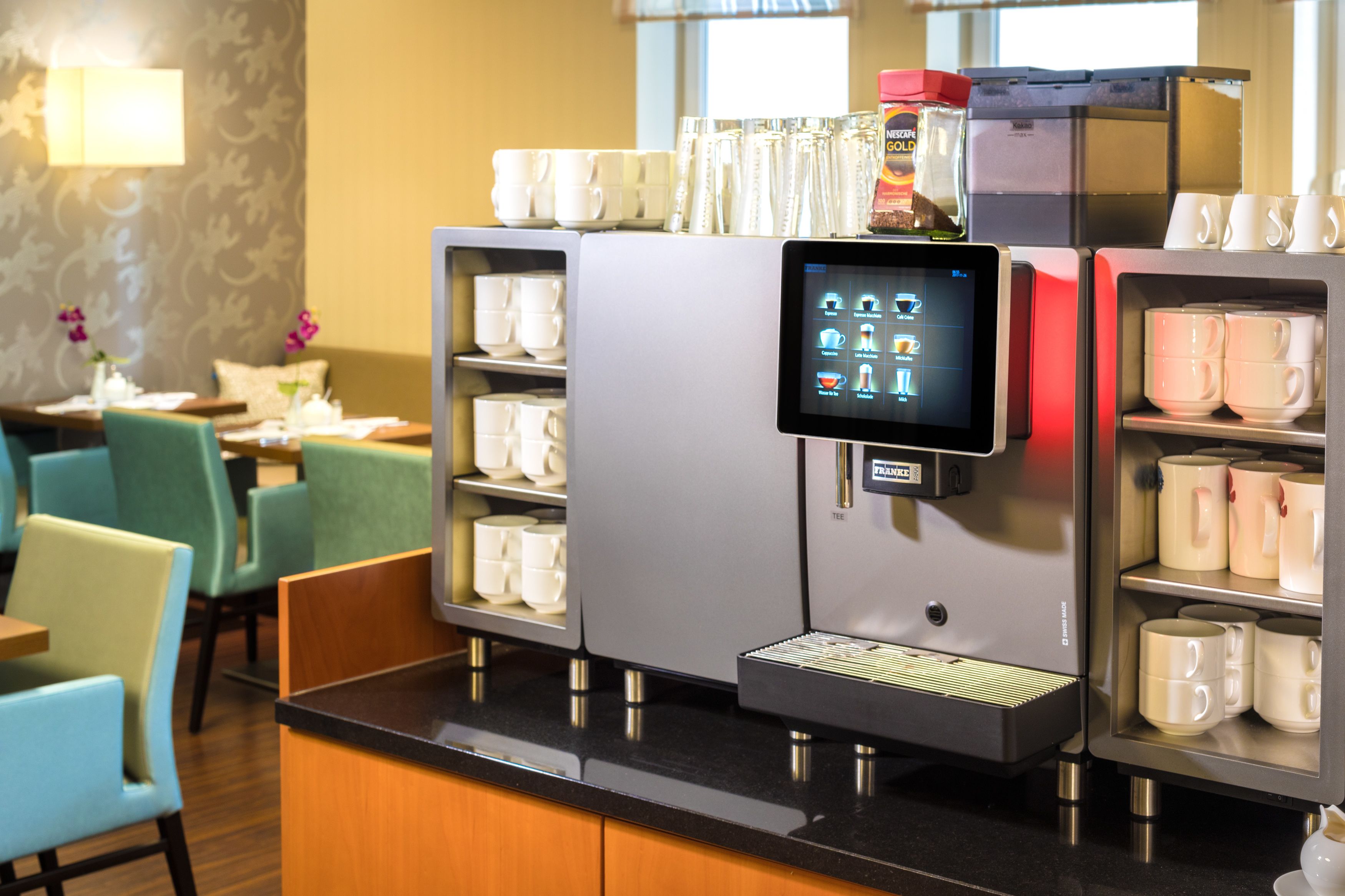 A coffee machine with a digital interface, surrounded by shelves of white and pink cups.