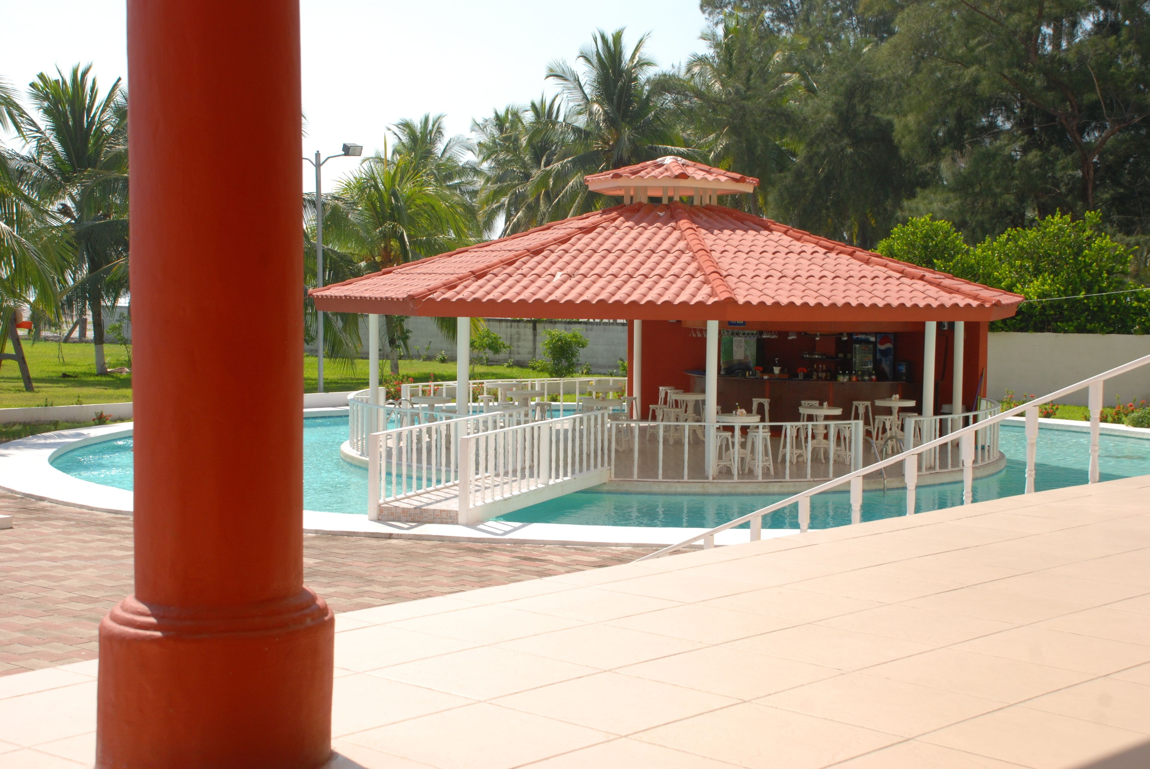 A pool area with a gazebo, white outdoor furniture, and palm trees in the background.