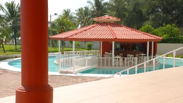 A pool area with a gazebo, white outdoor furniture, and palm trees in the background.