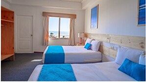 Habitación de hotel con dos camas, un armario de madera, un ventanal con vistas y un cuadro en la pared.