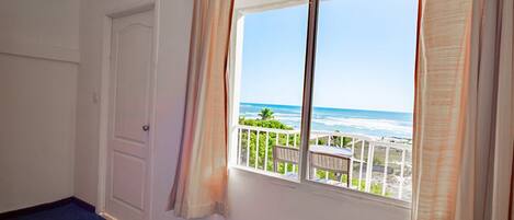 A room with a large window overlooking a beach, a door, and a blue carpet.