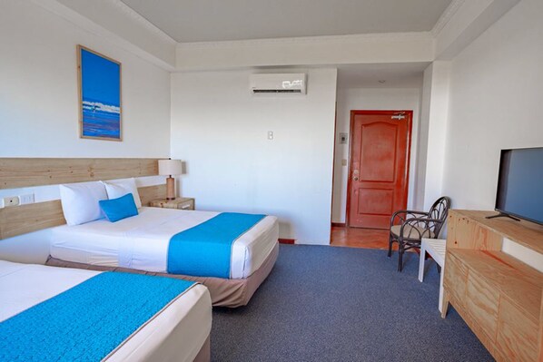 A hotel room with two beds, a TV, a desk, and a door leading to another room.