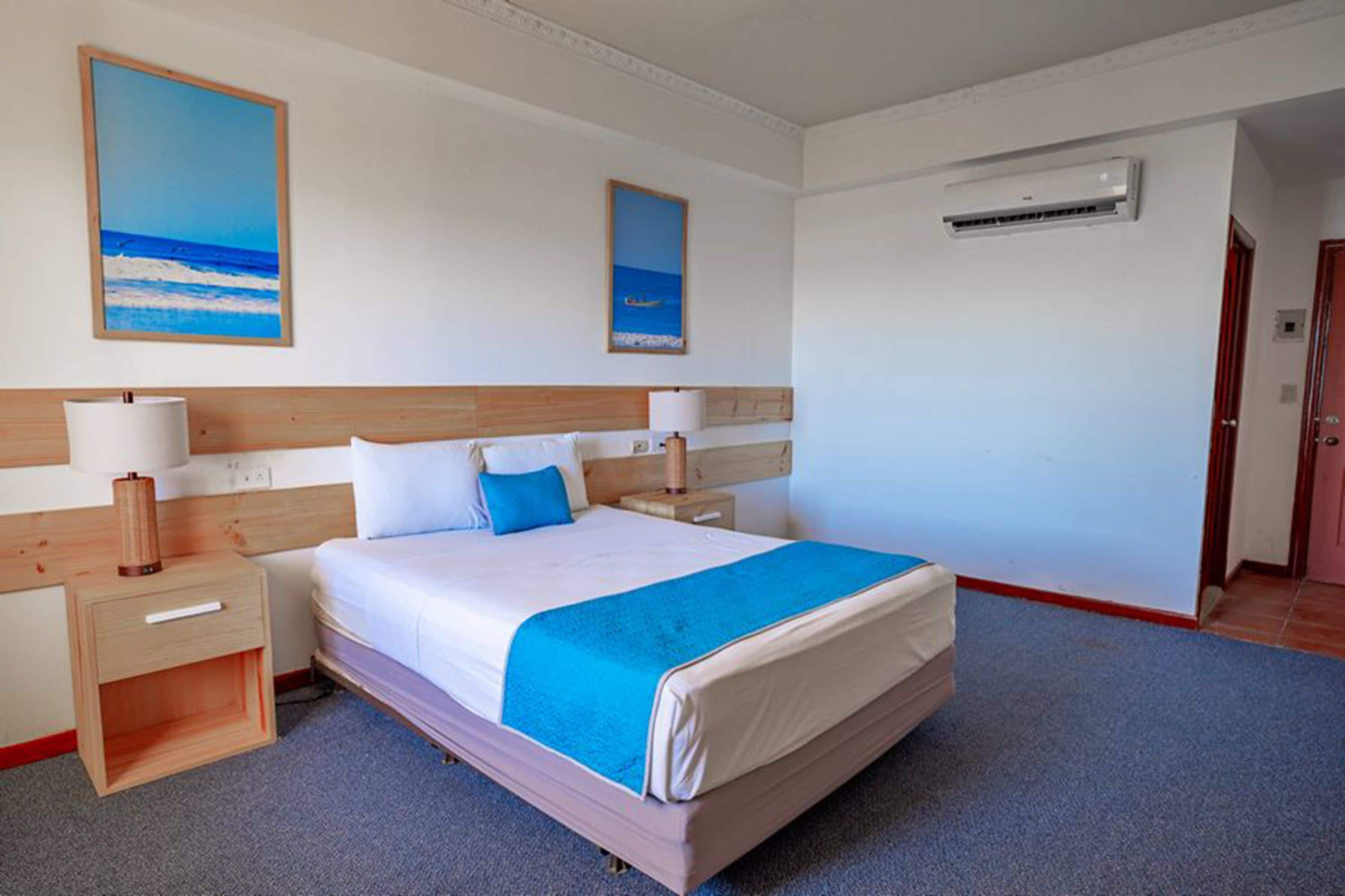 A hotel room with a large bed, two bedside tables with lamps, a wooden headboard, and two paintings on the wall.
