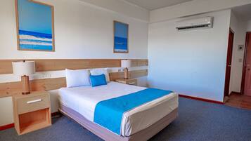 A hotel room with a large bed, two bedside tables with lamps, a wooden headboard, and two paintings on the wall.