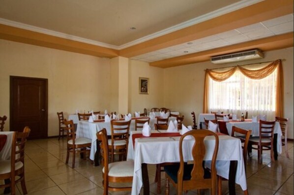 A dining area with multiple tables and chairs, an air conditioning unit, and a door.