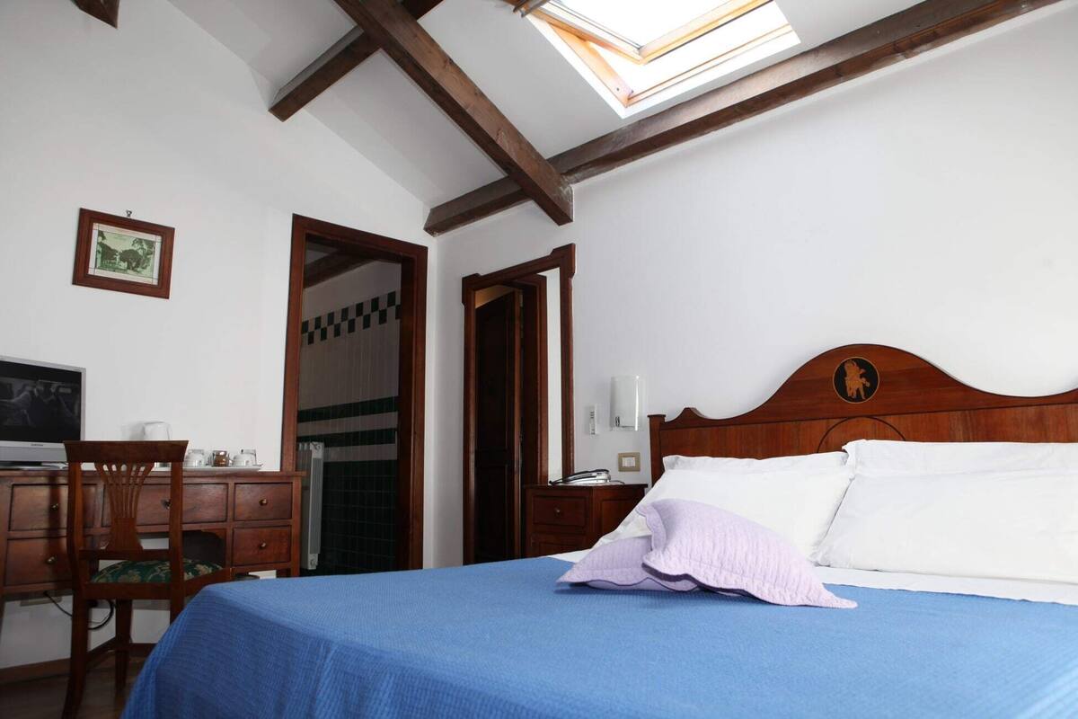 Une chambre à coucher avec un lit, un bureau avec un ordinateur, une chaise et une fenêtre donnant sur le ciel.