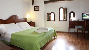 Un dormitorio con una cama de madera, un escritorio con una silla, un televisor y dos ventanas de arco.