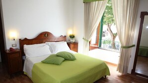Una cama bien hecha con ropa de cama blanca y verde, un cabecero de madera y una mesita de noche con un teléfono rojo.