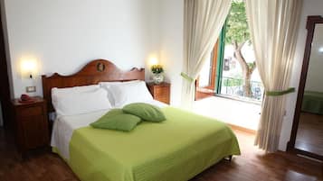 Un letto rifatto con lenzuola bianche e verdi, una testiera in legno e un comodino con un telefono rosso.