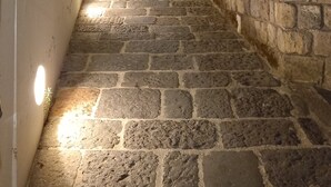 Una escalera de piedra que sube una colina, con un muro de ladrillo a un lado y un edificio blanco al otro.