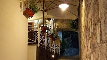 Un vialetto in pietra conduce a un edificio con facciata bianca e una zona relax esterna coperta, adornata con piante pendenti.