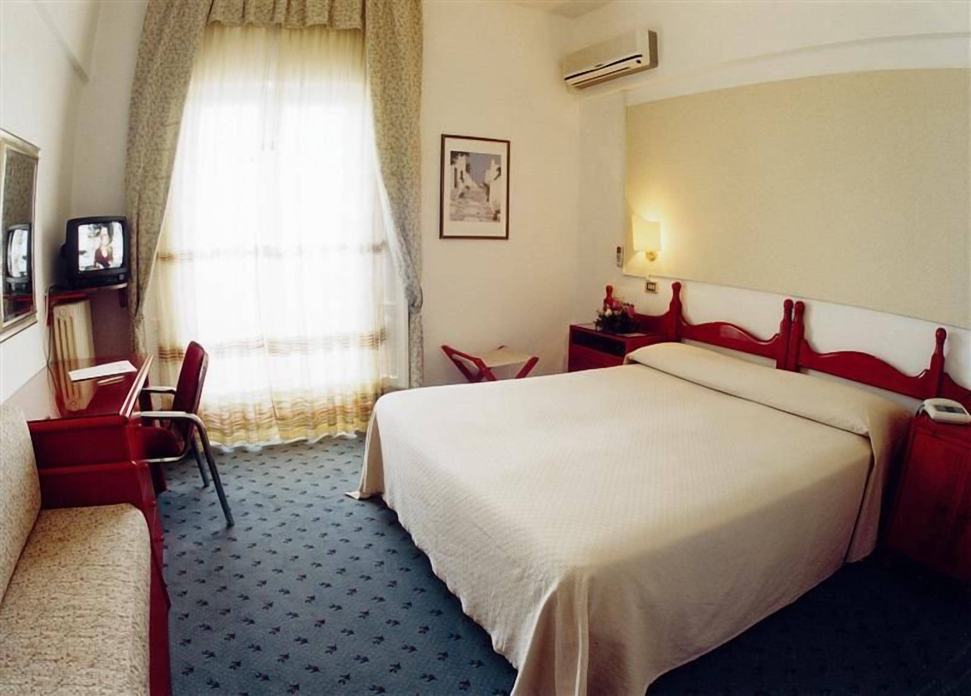 Een hotelkamer met een bed, een bureau met stoel, een televisie en een raam met gordijnen.