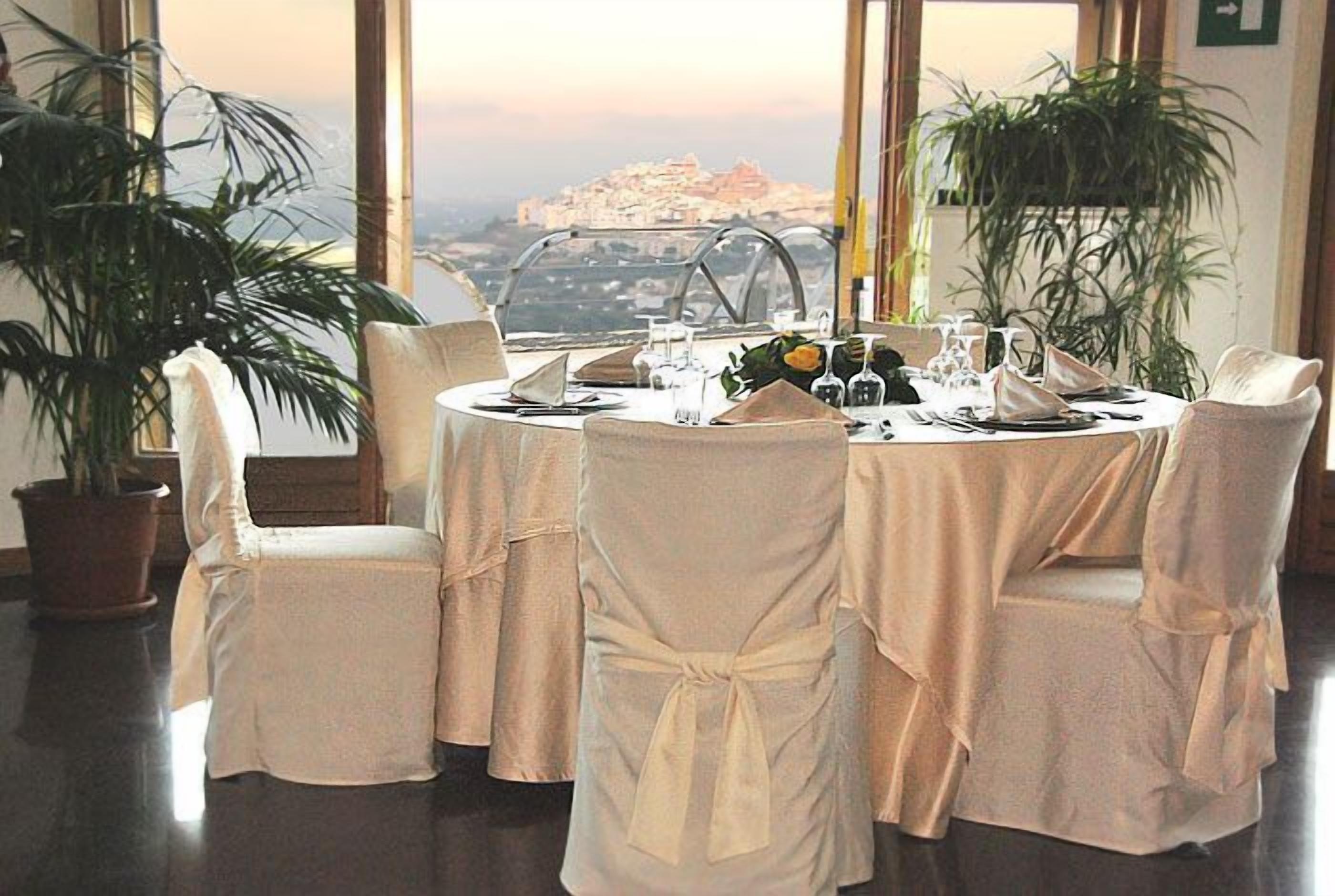 Une table de salle à manger ronde, recouverte d’une nappe blanche, avec des chaises, mise pour un repas avec des assiettes, des verres et des couverts.