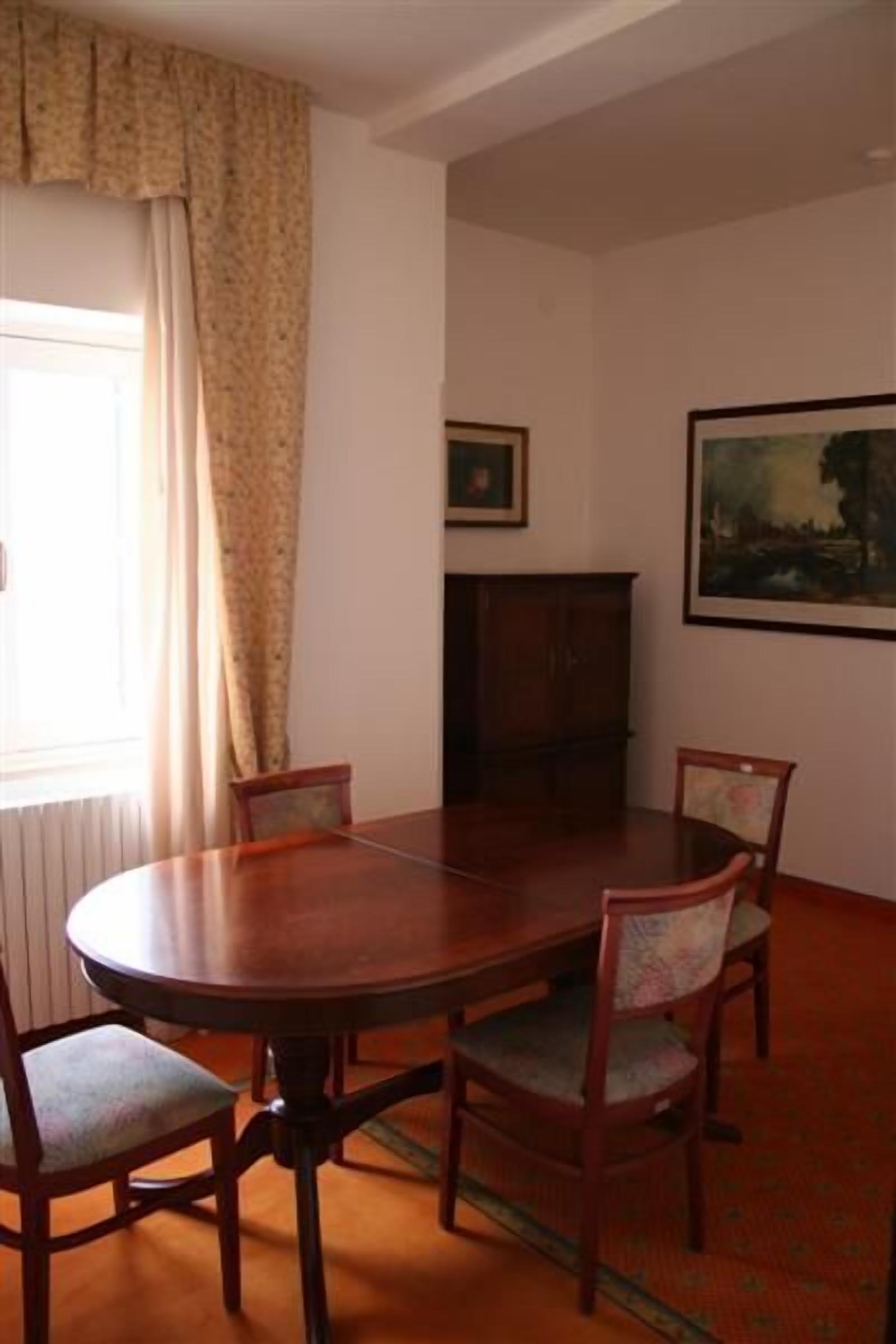 Ein Zimmer mit einem runden Holztisch, vier Stühlen, einer Kommode und zwei gerahmten Bildern an der Wand.