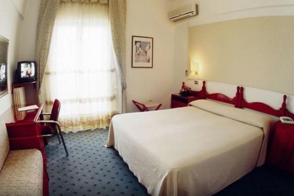 A hotel room with a bed, a desk, a chair, and a television.