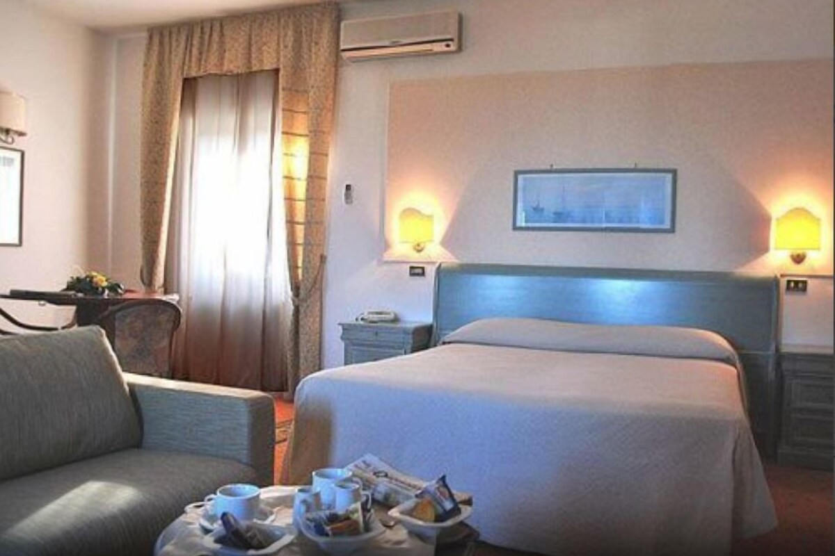 Habitación de hotel con cama, sofá, mesa con alimentos para el desayuno y dos lámparas de pared.