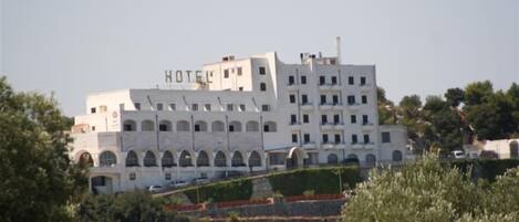 Een groot, wit hotel met meerdere verdiepingen en een opvallend “HOTEL”-bord aan de bovenkant.