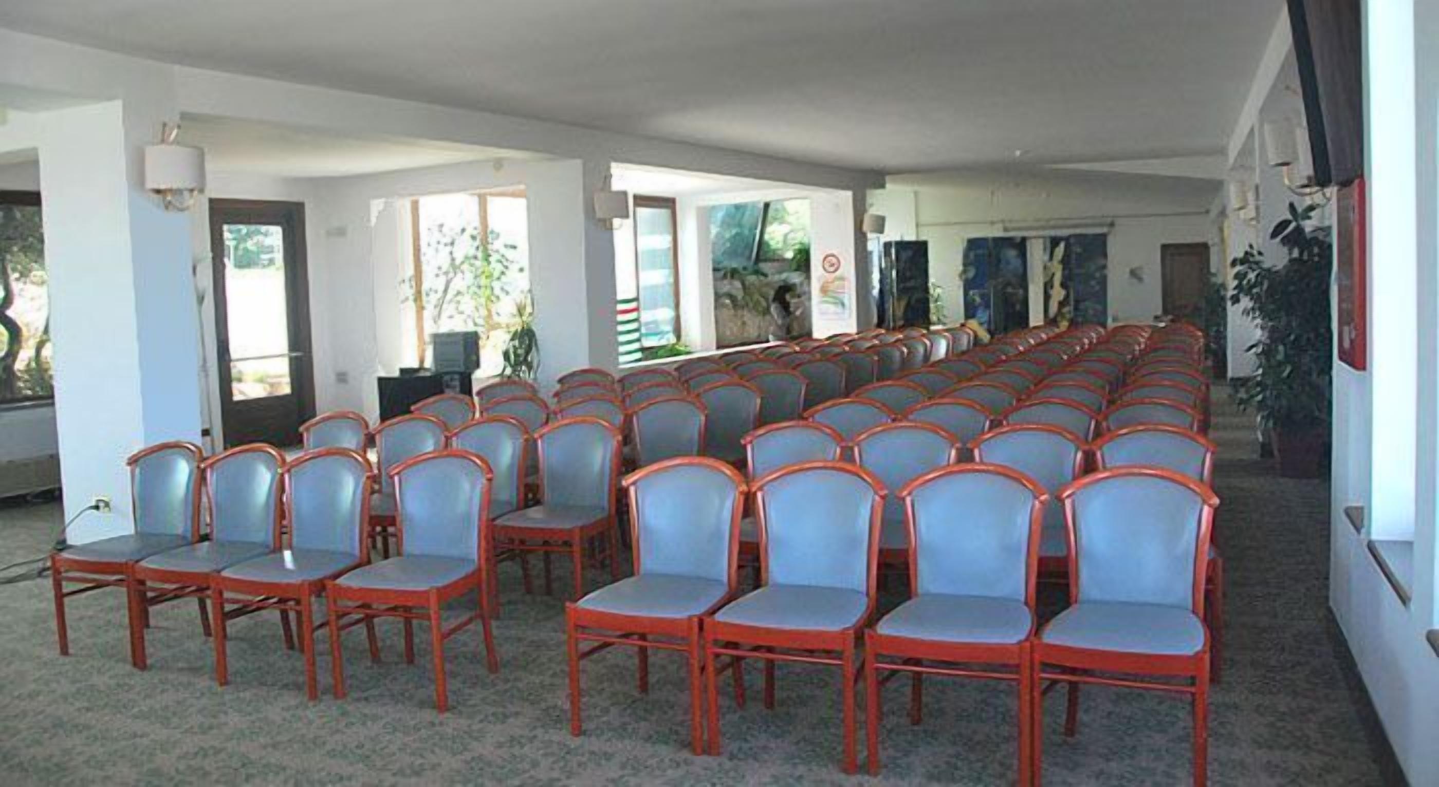 A conference room with rows of chairs and tables, large windows, and a view of the outdoors.