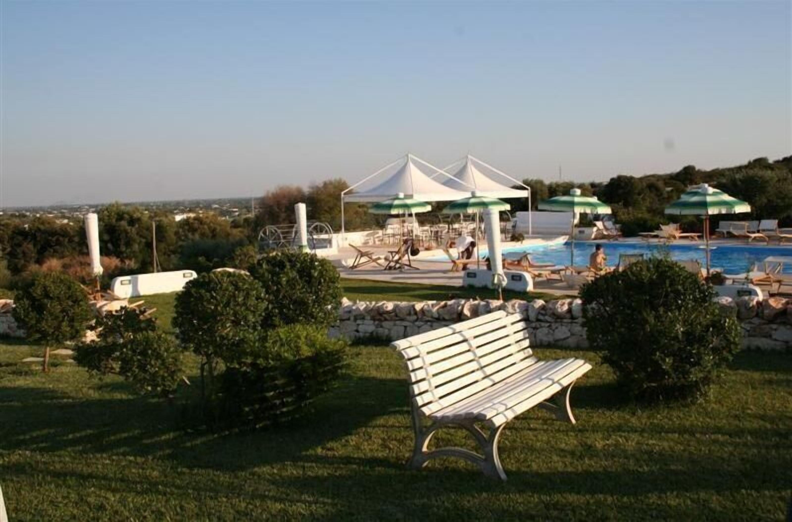 Un área de piscina con sombrillas, sillas de descanso y un banco.