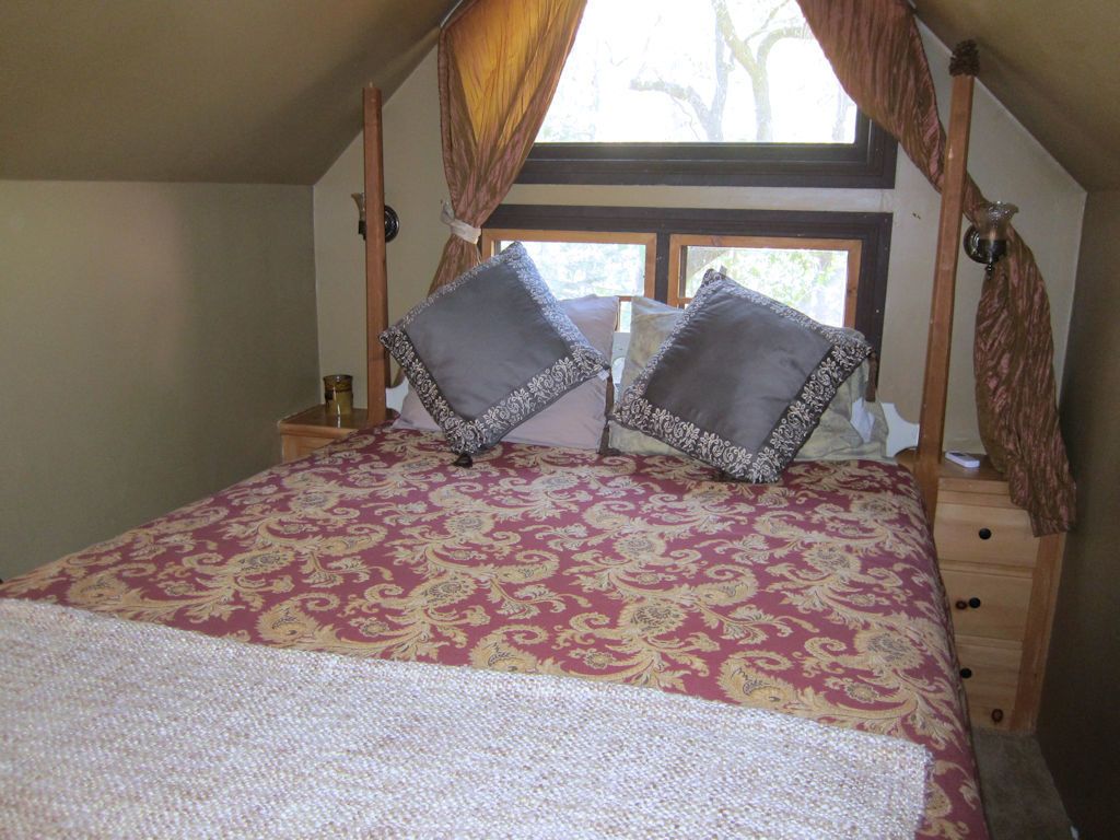 Une chambre à coucher avec un lit, deux oreillers, une table de chevet, une fenêtre et des rideaux.
