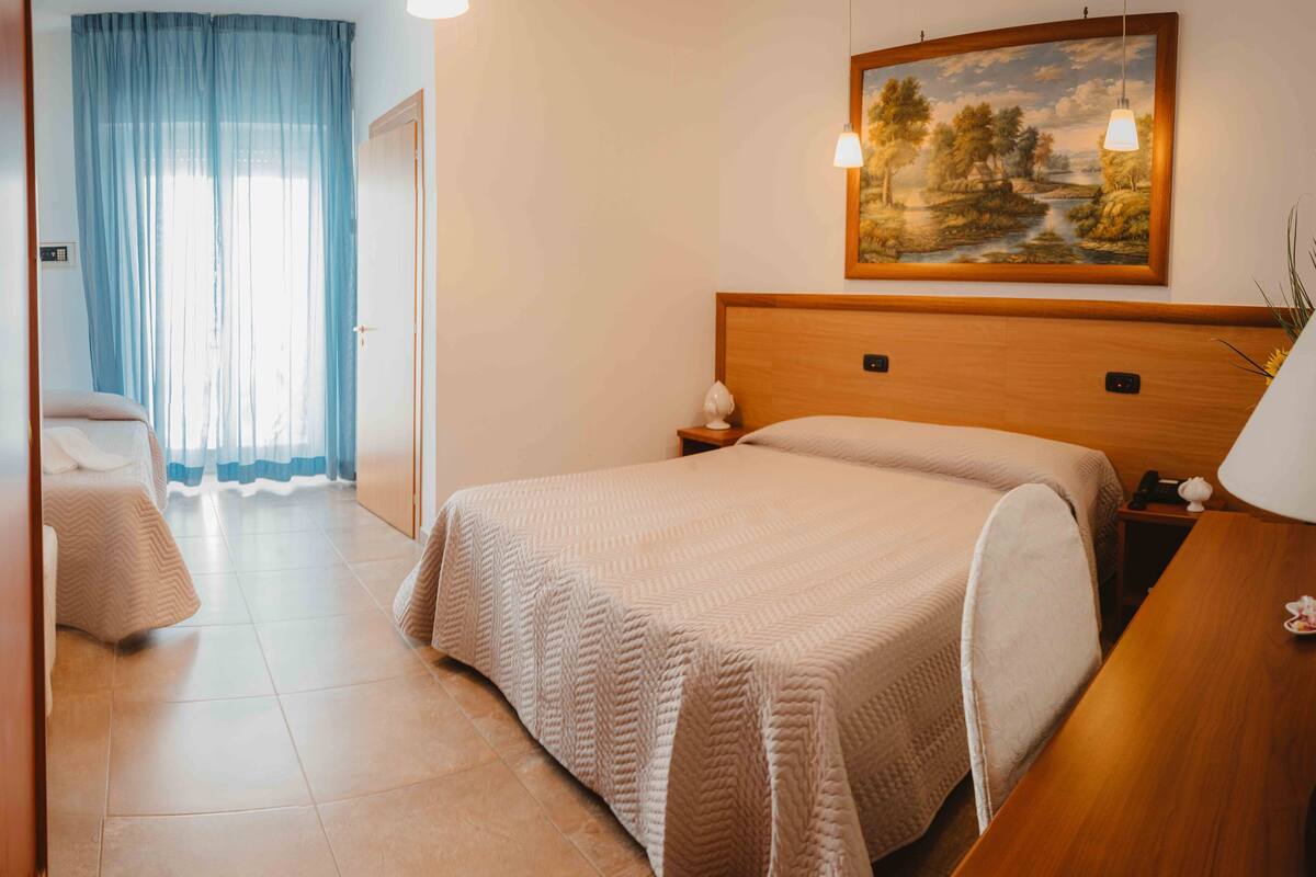 Hotelkamer met een groot bed, een nachtkastje, een schilderij aan de muur en een raam met gordijnen.