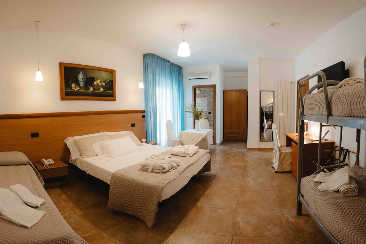 Een hotelkamer met een bed, een bureau, een spiegel, een stapelbed en een schilderij aan de muur.