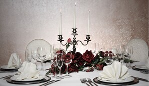 Une table à manger élégante, recouverte d’une nappe blanche, avec de l’argenterie, des assiettes et un chandelier orné de bougies.