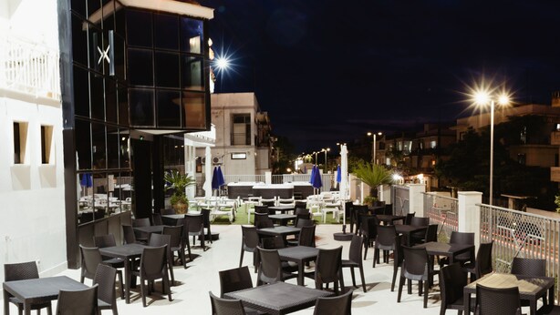 Een terras met tafels en stoelen, een gebouw met grote ramen en een uitzicht op de stad 's nachts.