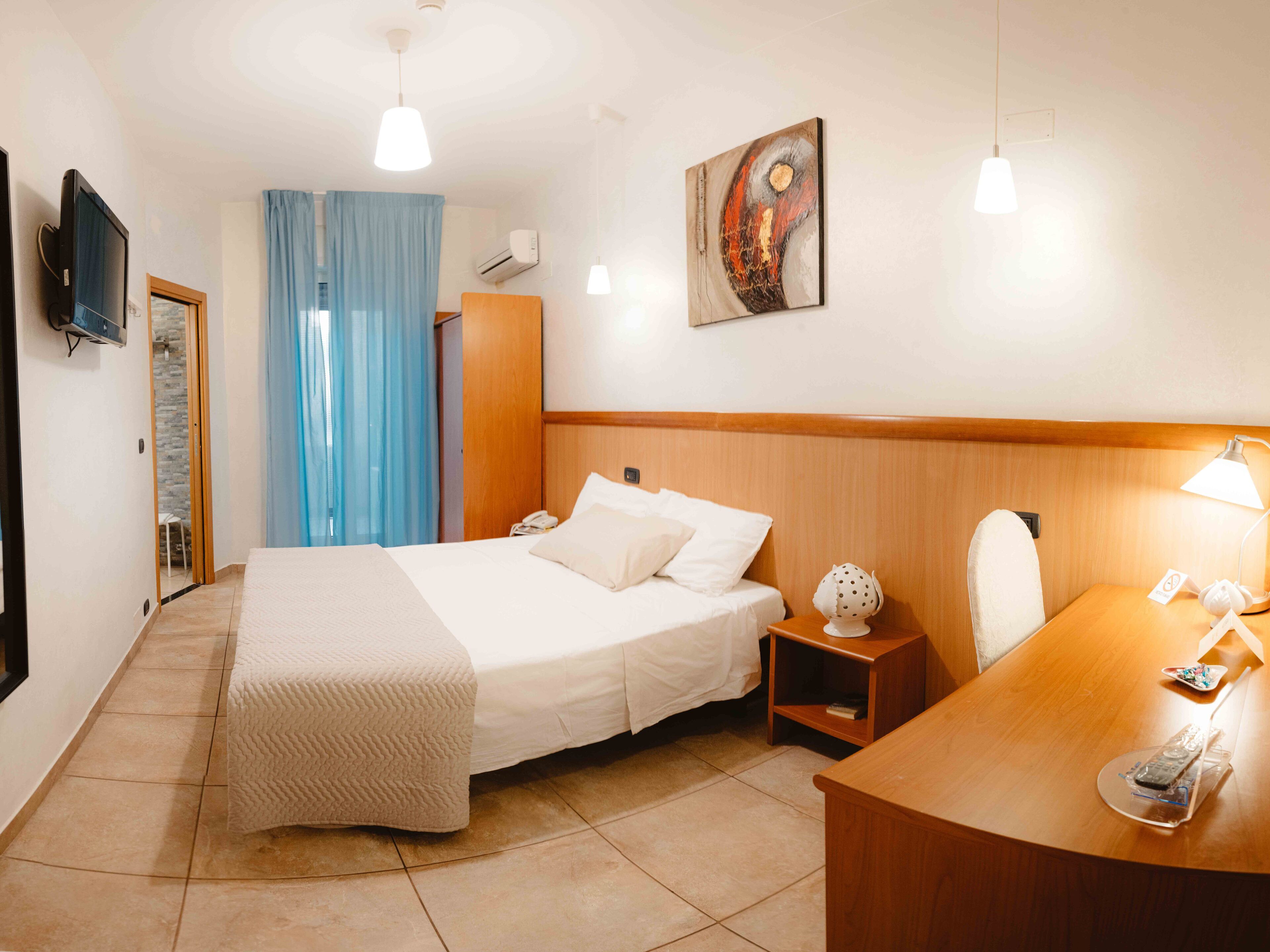A hotel room with a bed, bedside table, desk, chair, and a television on the wall.