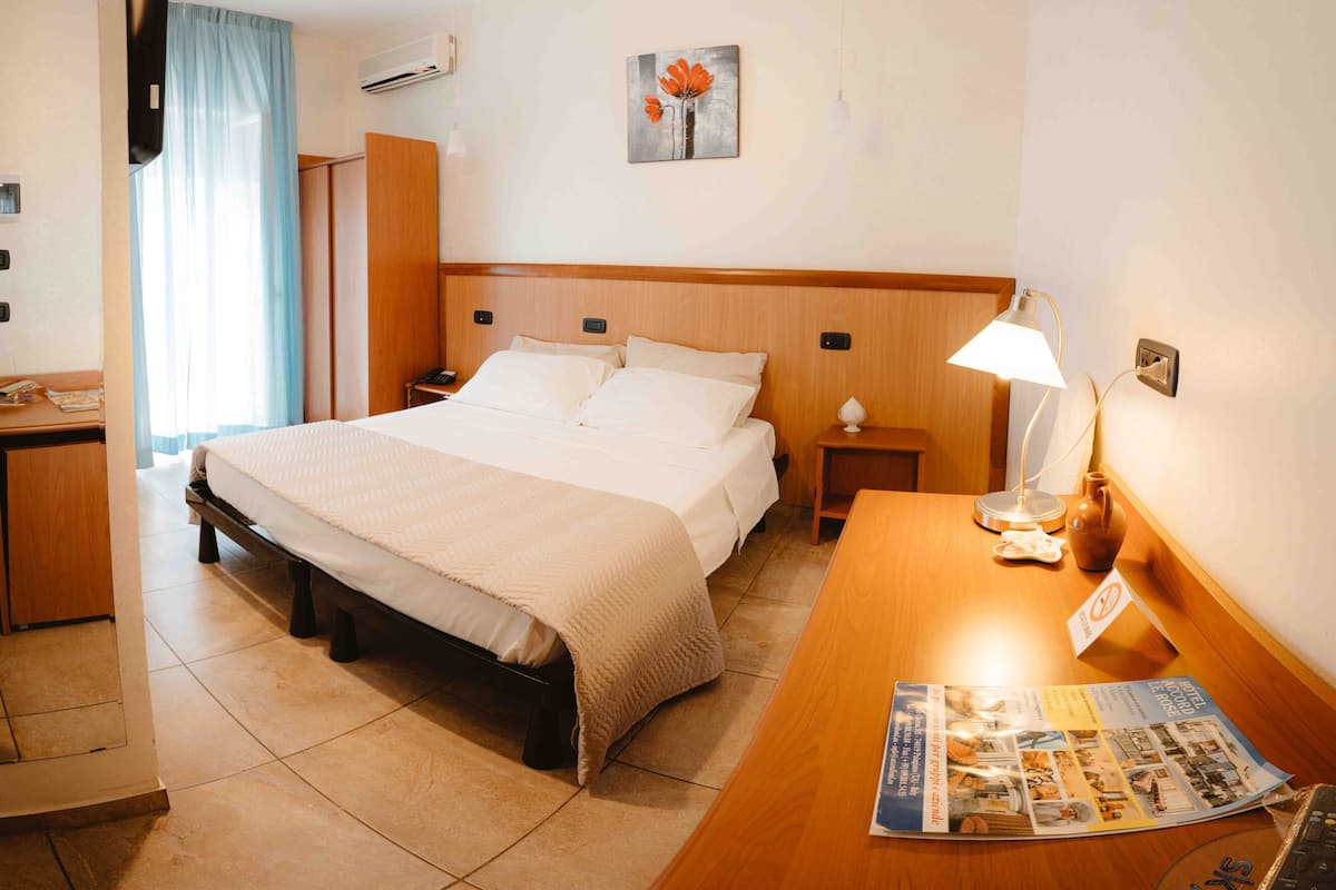 Een hotelkamer met een bed, nachtkastjes, een bureau, een lamp, een schilderij en een raam met gordijnen.