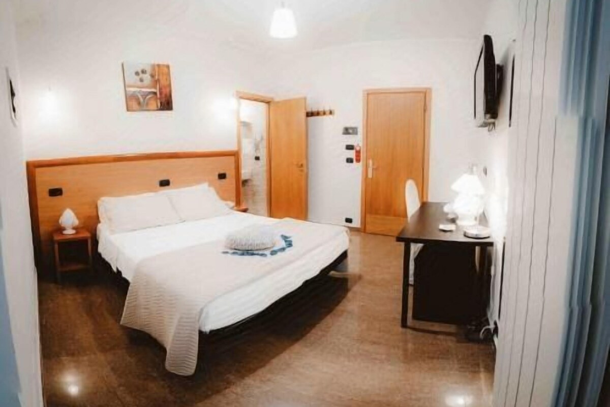 Une chambre d’hôtel avec un lit, une table de chevet, une lampe et un téléviseur fixé au mur.
