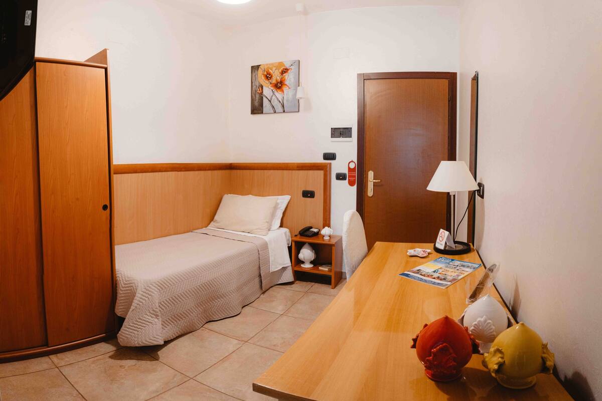 Een kleine, verzorgde kamer met een bed, een bureau, een lamp en een deur.