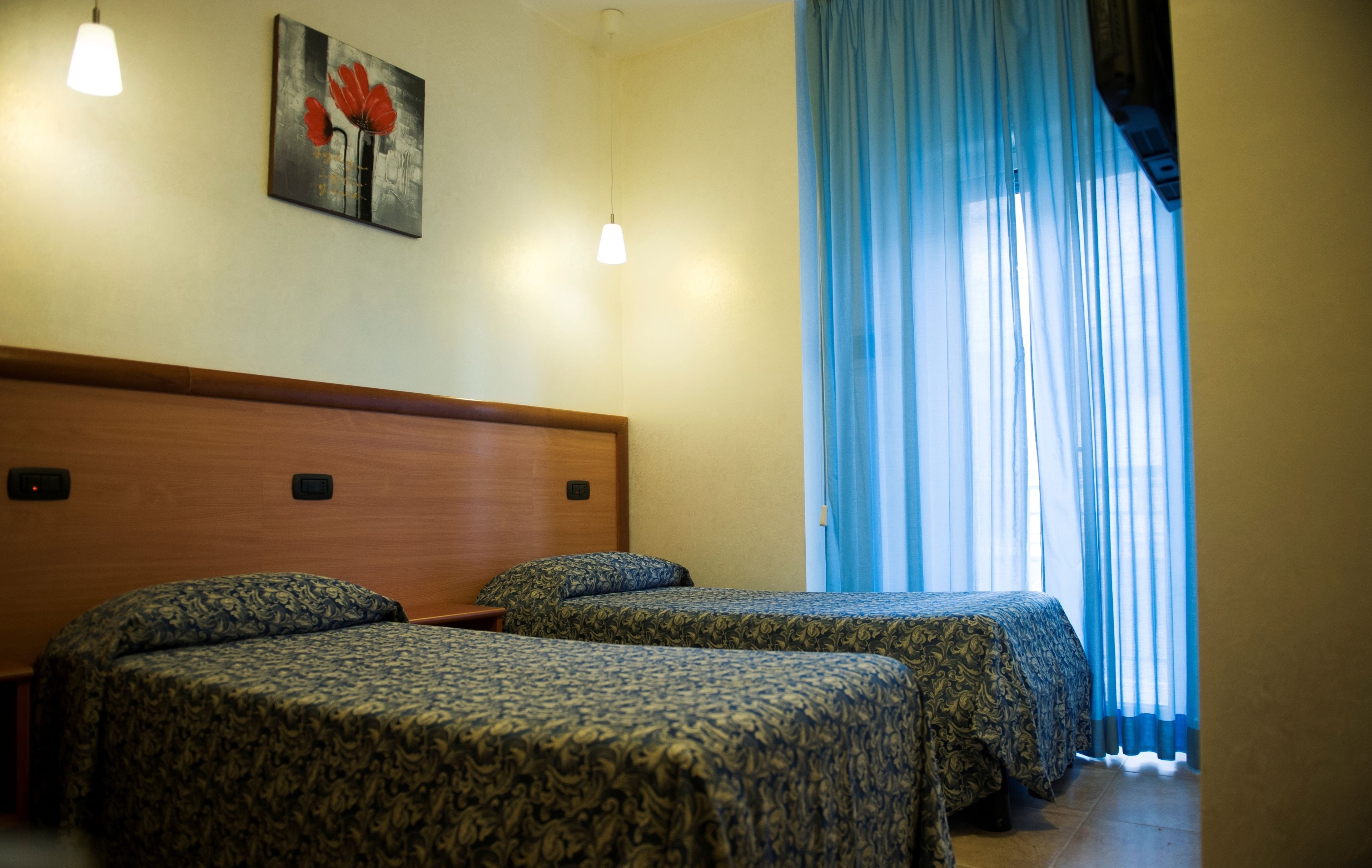Habitación de hotel con dos camas, cabecera de madera, un cuadro en la pared y una ventana con cortinas azules.