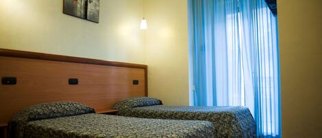 Habitación de hotel con dos camas, cabecera de madera, un cuadro en la pared y una ventana con cortinas azules.
