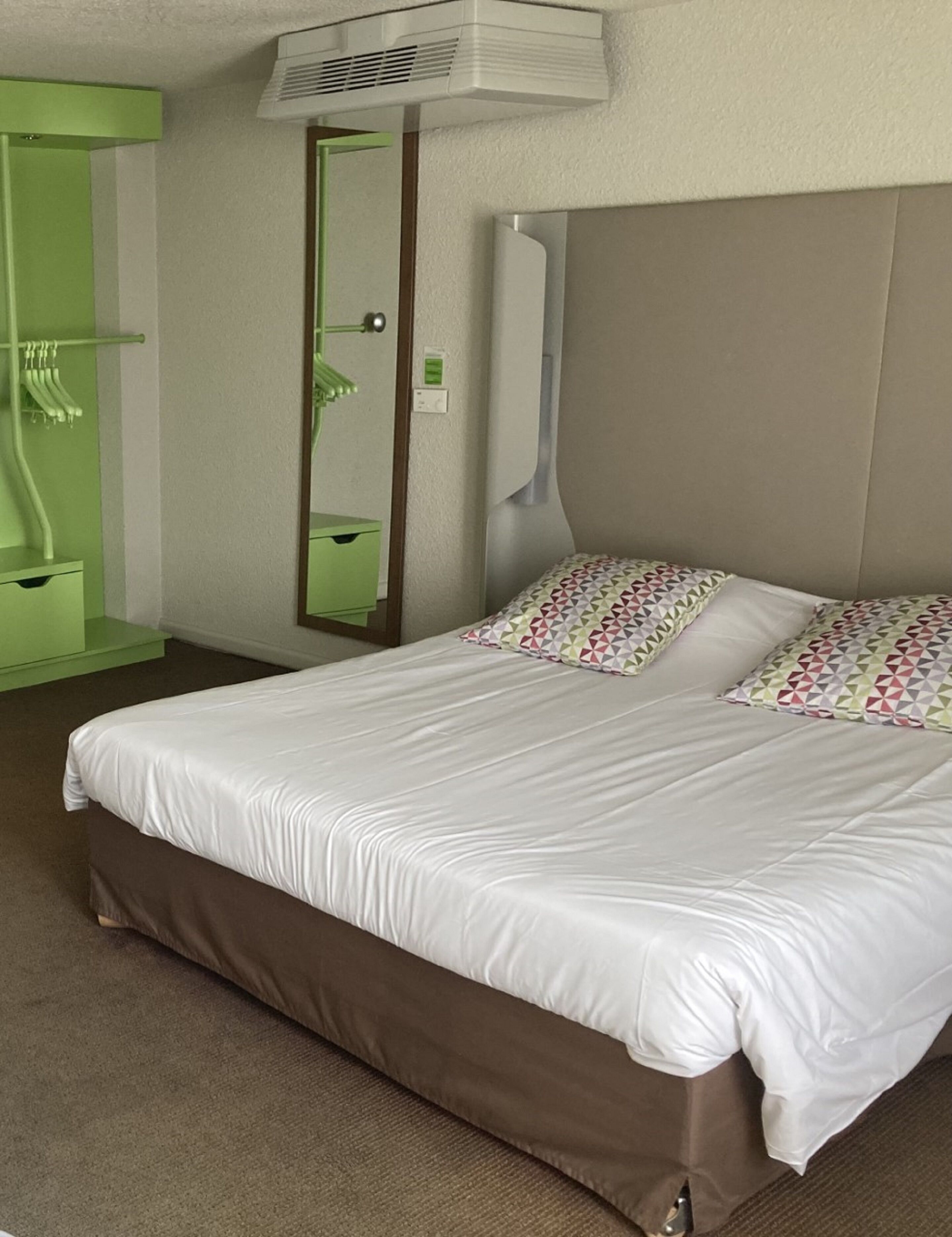 Una camera d'albergo con un letto, uno specchio, un bagno verde e un condizionatore d'aria.