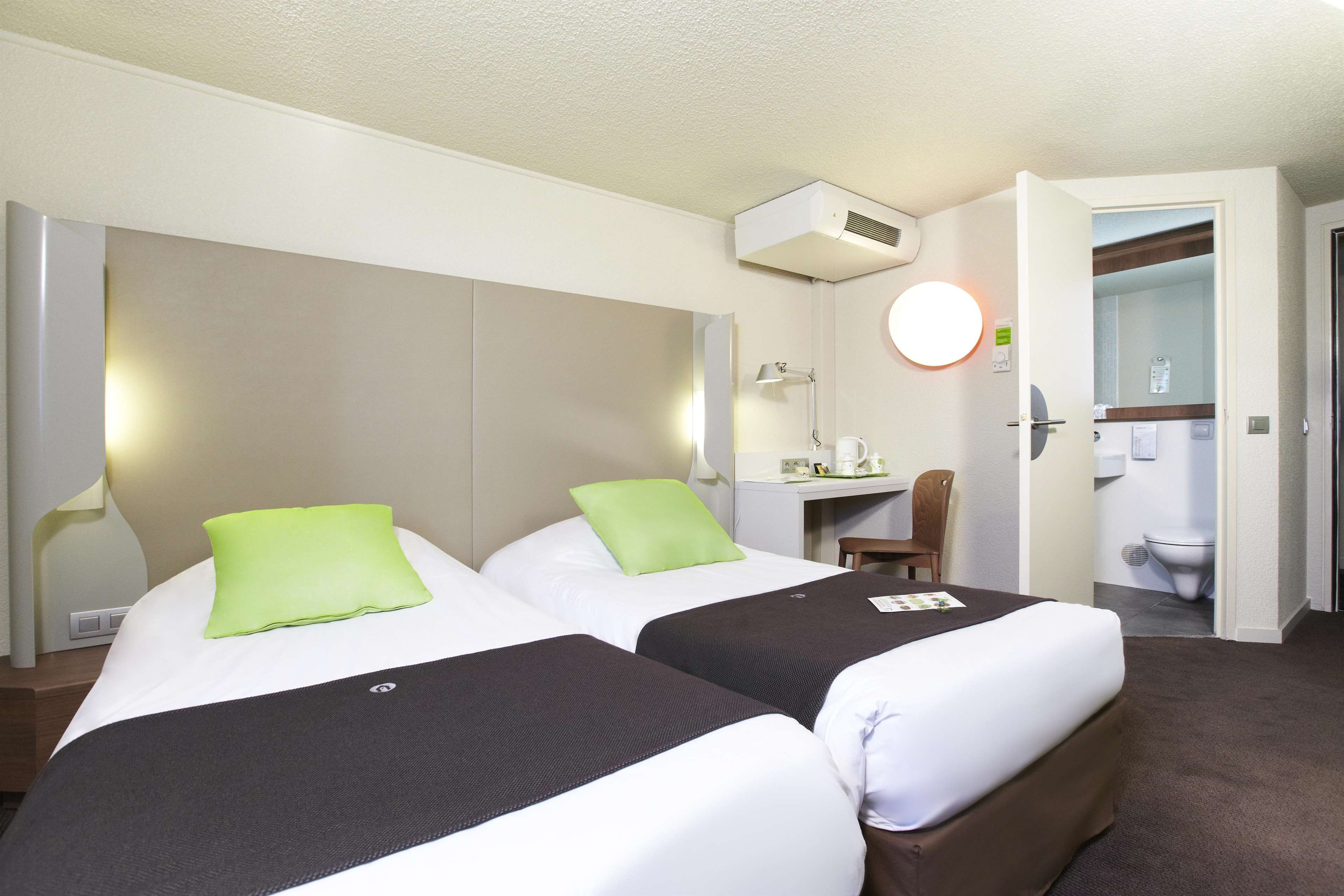 A hotel room with two beds, a desk, a chair, a toilet, and a mirror.