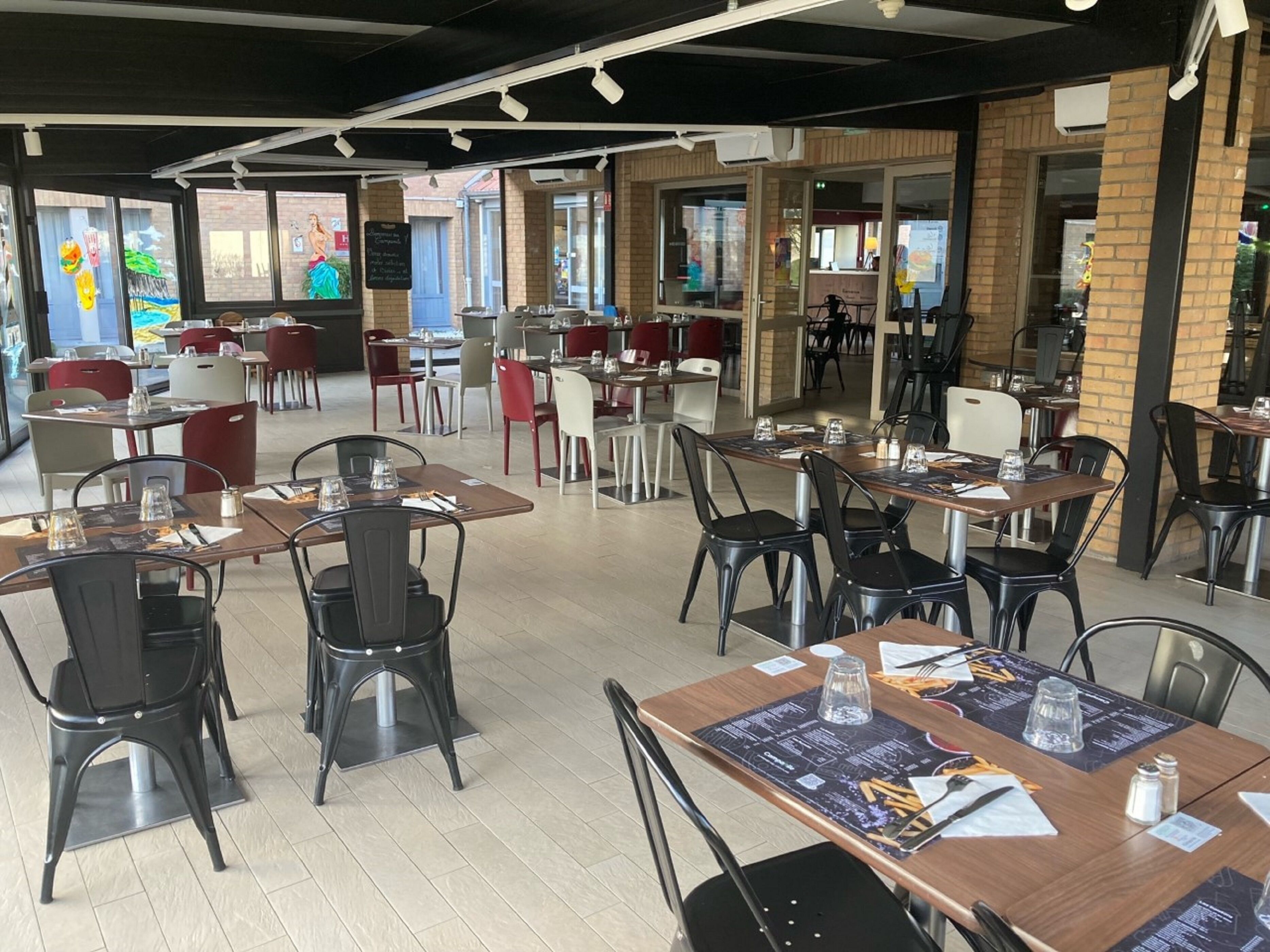 Un vaste espace de restauration intérieur, doté de nombreuses tables et chaises, de grandes fenêtres et d’un design moderne.