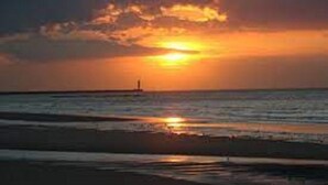 Atardecer sobre el océano con un faro a lo lejos.