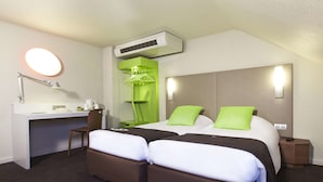 Habitación de hotel con escritorio, dos camas con almohadas verdes, una silla, perchero y equipo de aire acondicionado.