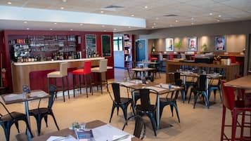 Een restaurant met meerdere tafels en stoelen, een bar met flessenrekken en een krijtbordmenu.