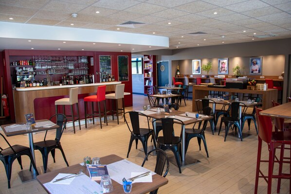 A restaurant with multiple tables and chairs, a bar area with shelves of bottles, and a chalkboard menu.
