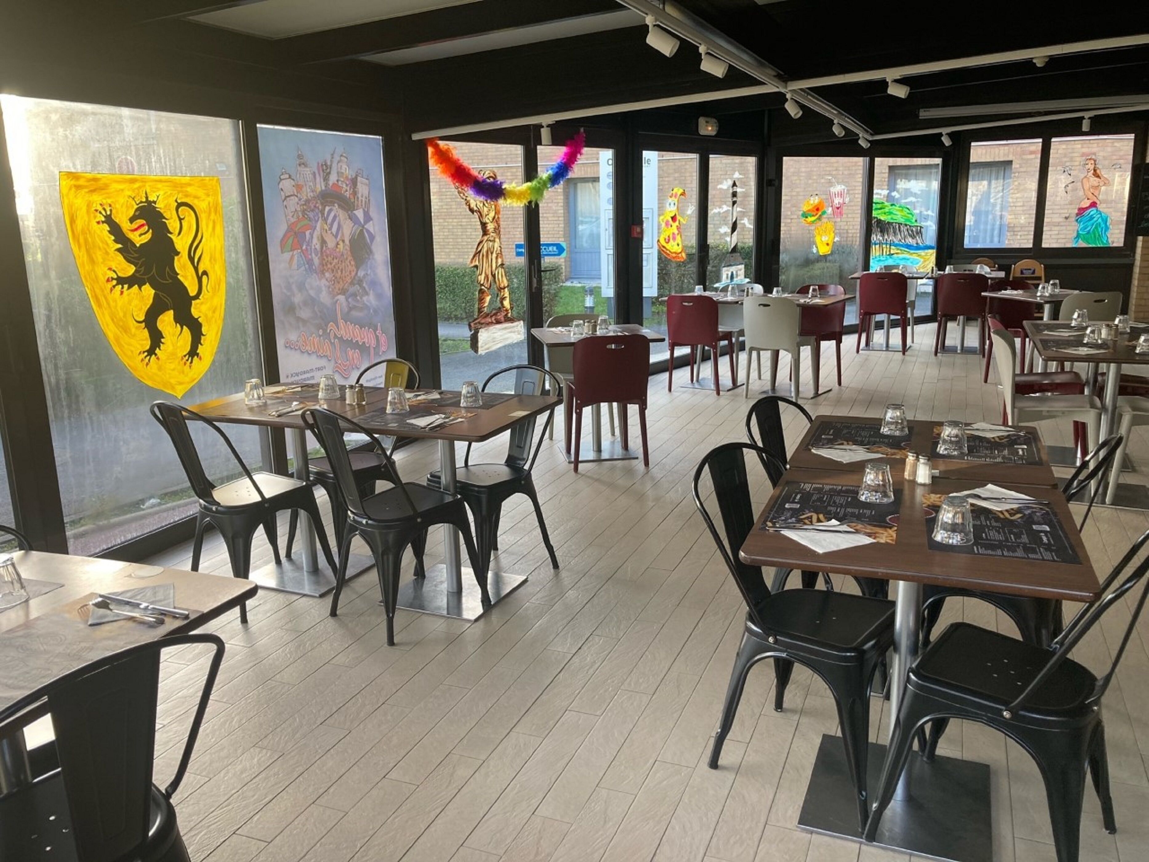 Un restaurant avec des tables et des chaises, de grandes fenêtres et des œuvres d’art accrochées aux murs.