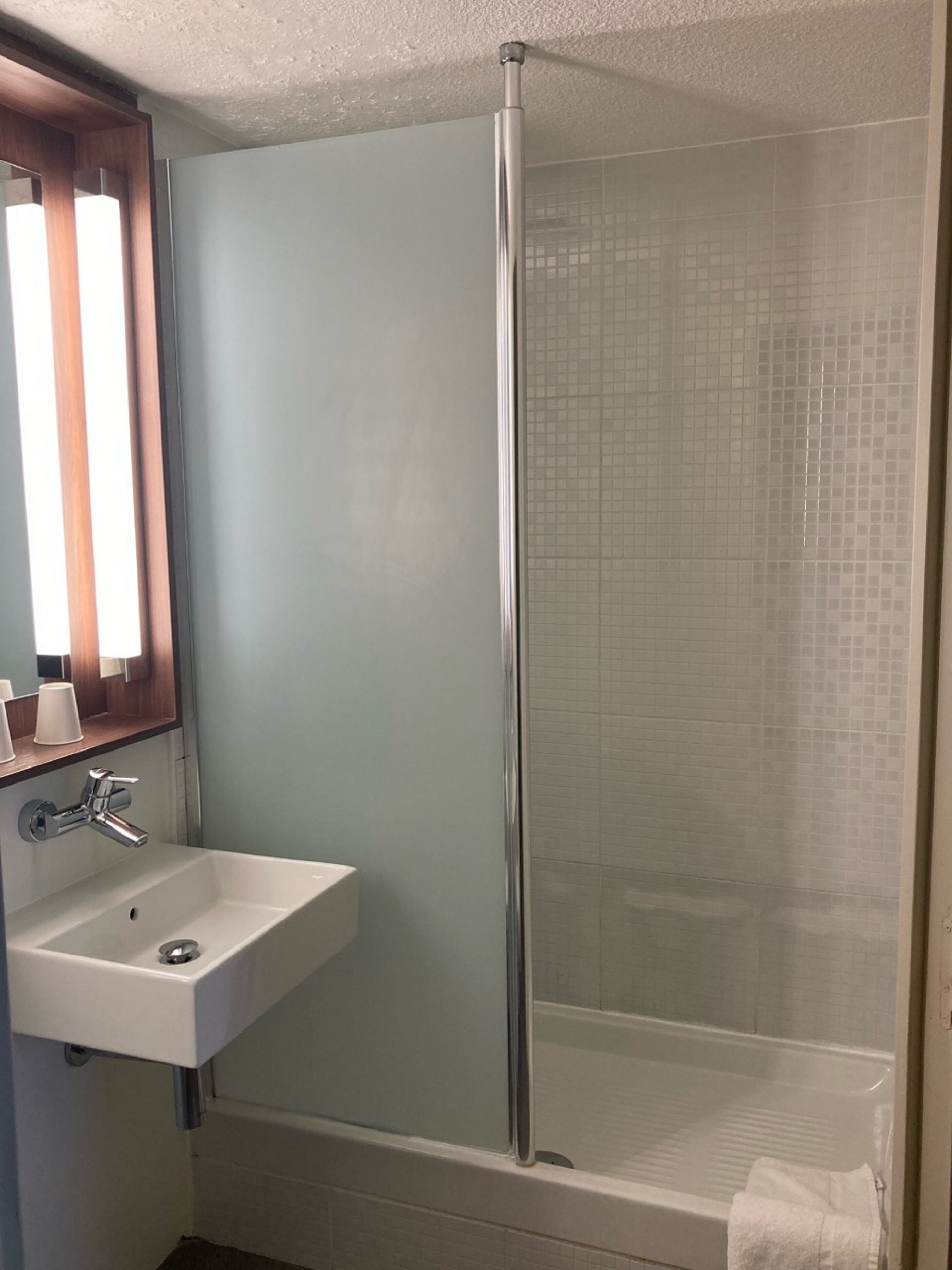 A bathroom with a glass shower enclosure, a sink with a mirror, and a towel rack.